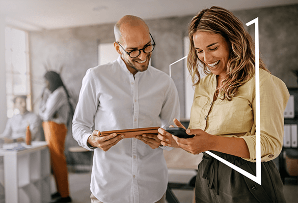 a business man and business woman work collaboratively while looking at technology surrounded by a white geometric shape